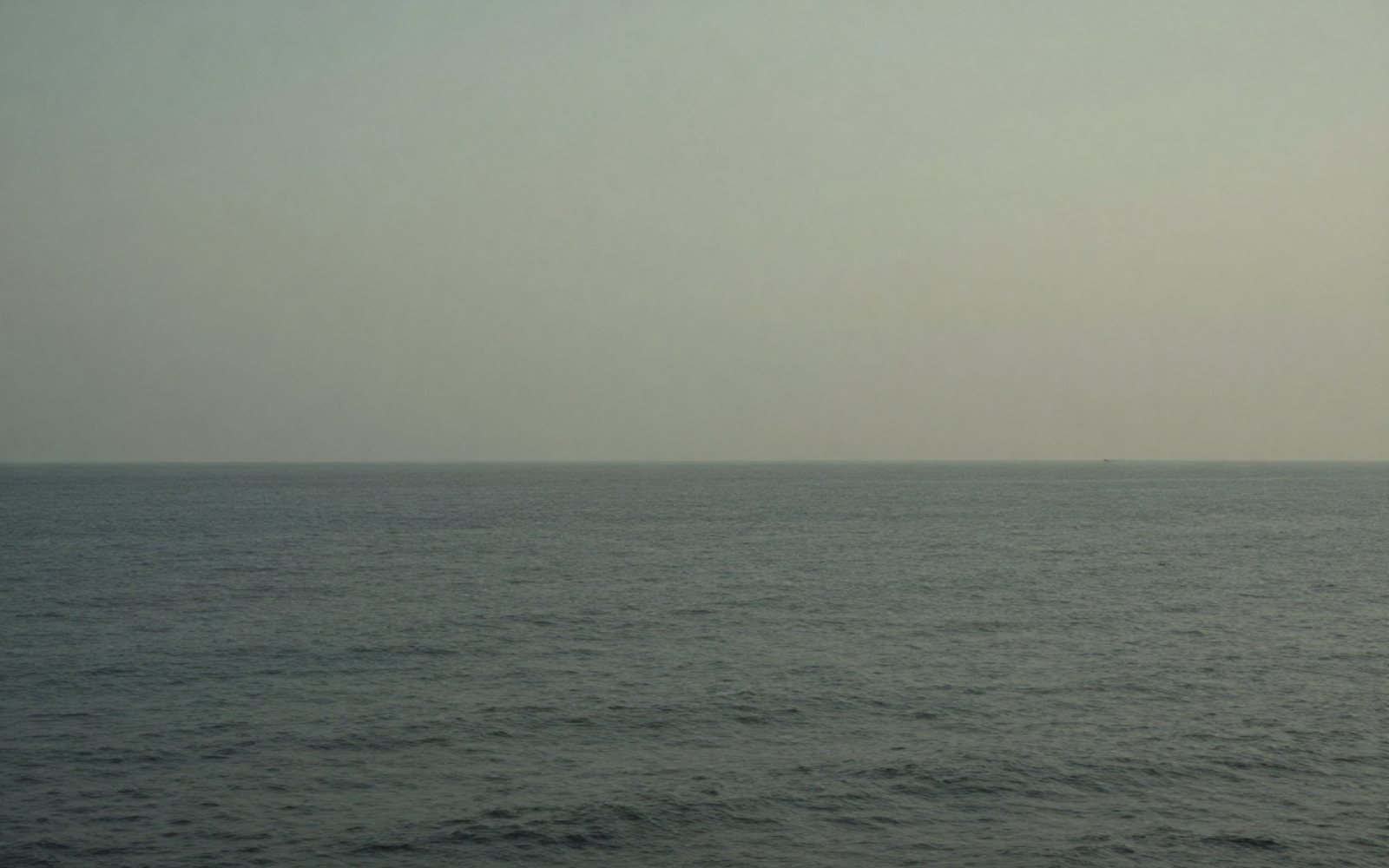 A calm, overcast sea meeting a hazy horizon.