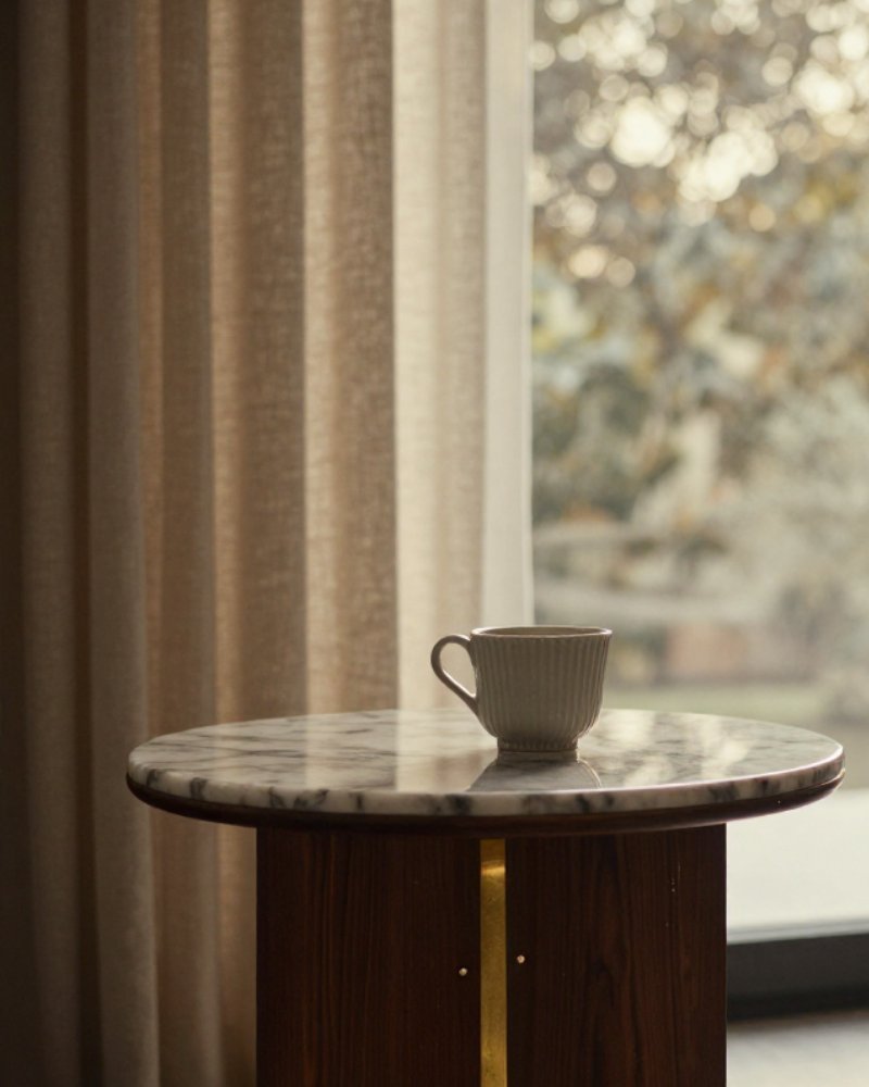 A marble side table with a ceramic cup, sheer curtains and soft morning window light.